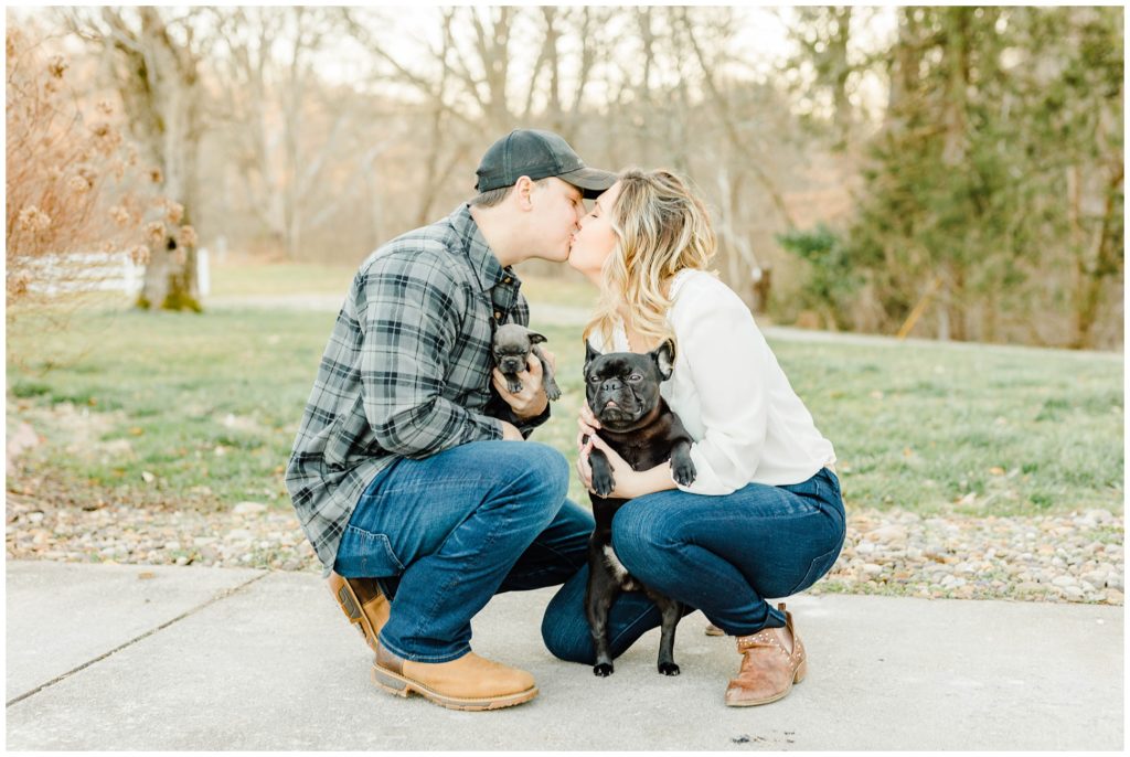 a recently engaged couple holds their french bulldog puppies while they kiss during their engagement pictures in Barboursville, WV