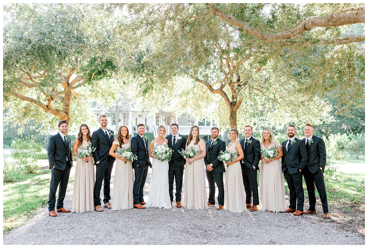 Newlyweds pose for photos with wedding party in navy suits and tan dresses at Old Wide Awake, a wedding venue in Charleston, SC