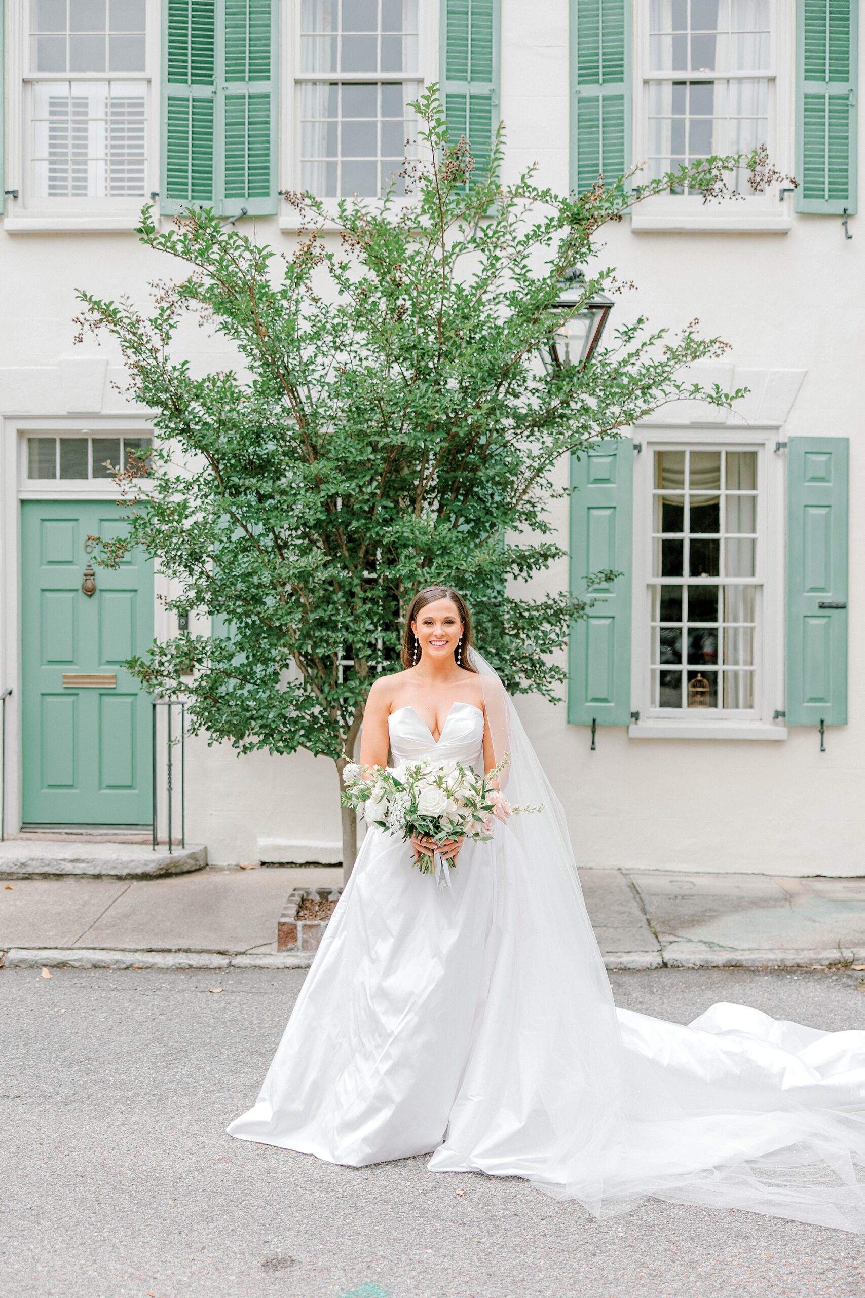 bride in strapless wedding gown holds bouquet of white flowers in front of homes on Rainbow Row