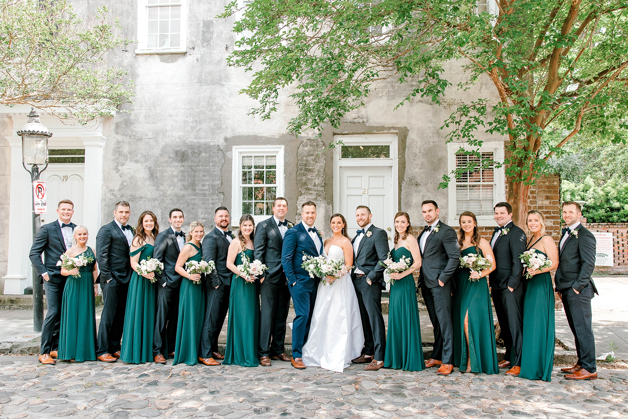 newlyweds pose with wedding party in green dresses and navy suits near The Cedar Room