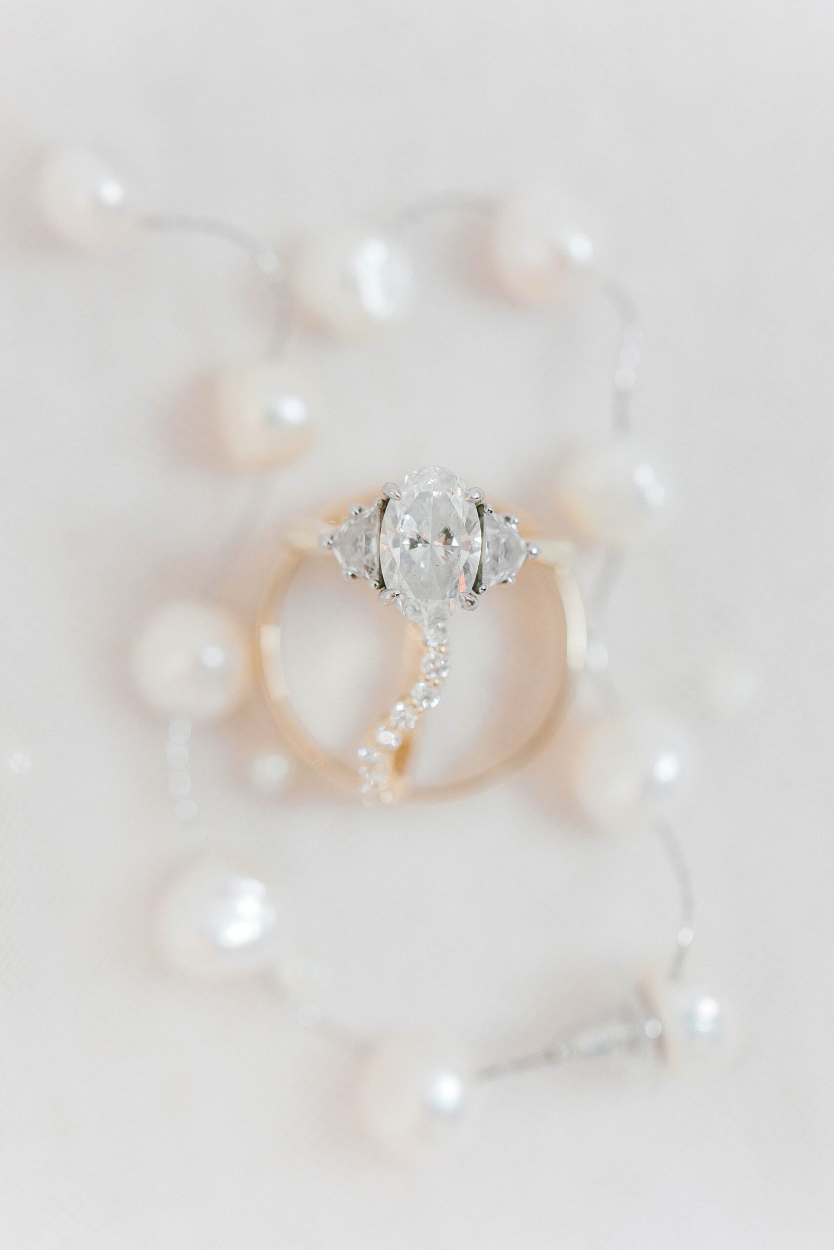 bride's gold rings rest between pearl bracelet 
