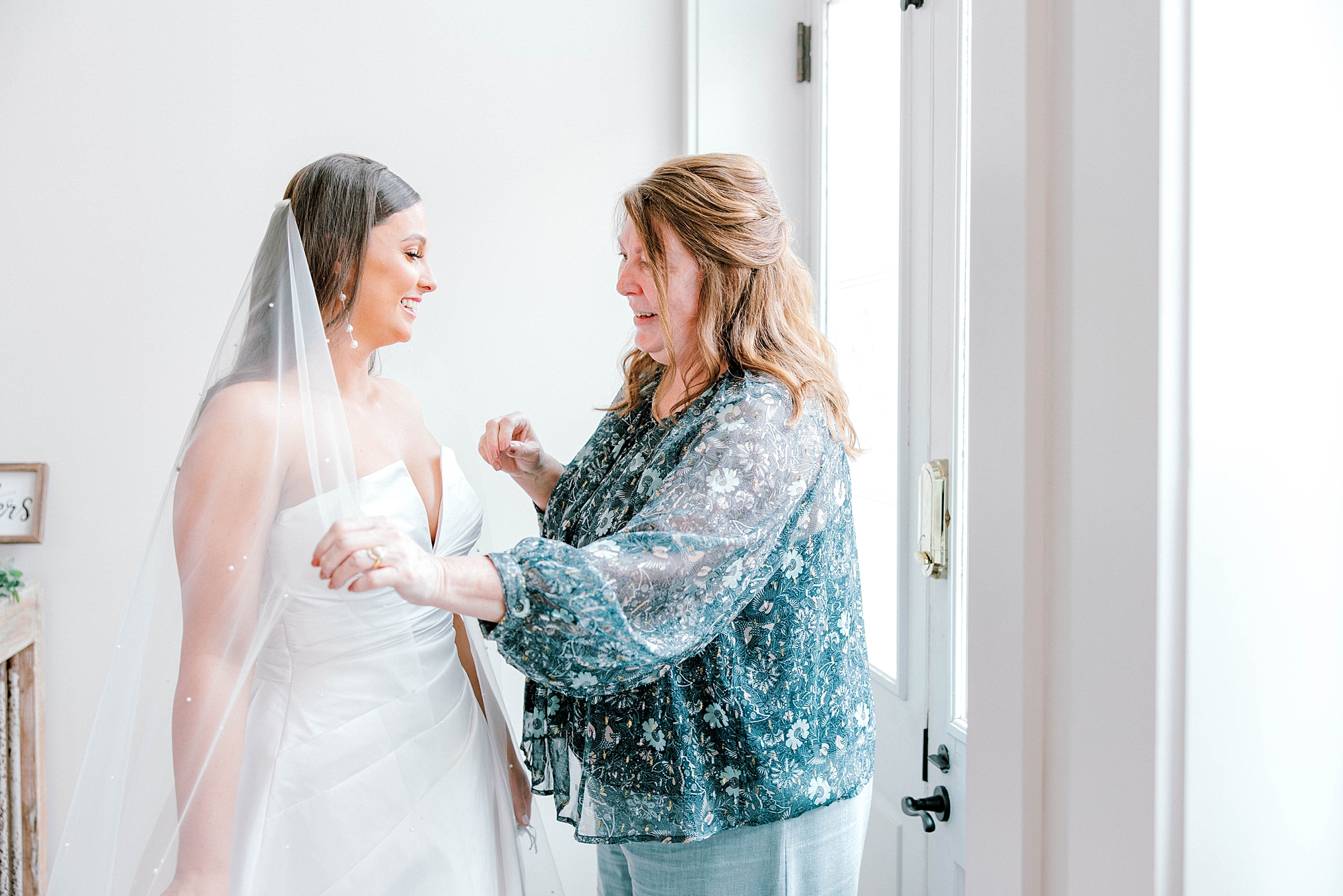 mother helps bride pull veil around shoulders before Charleston wedding 
