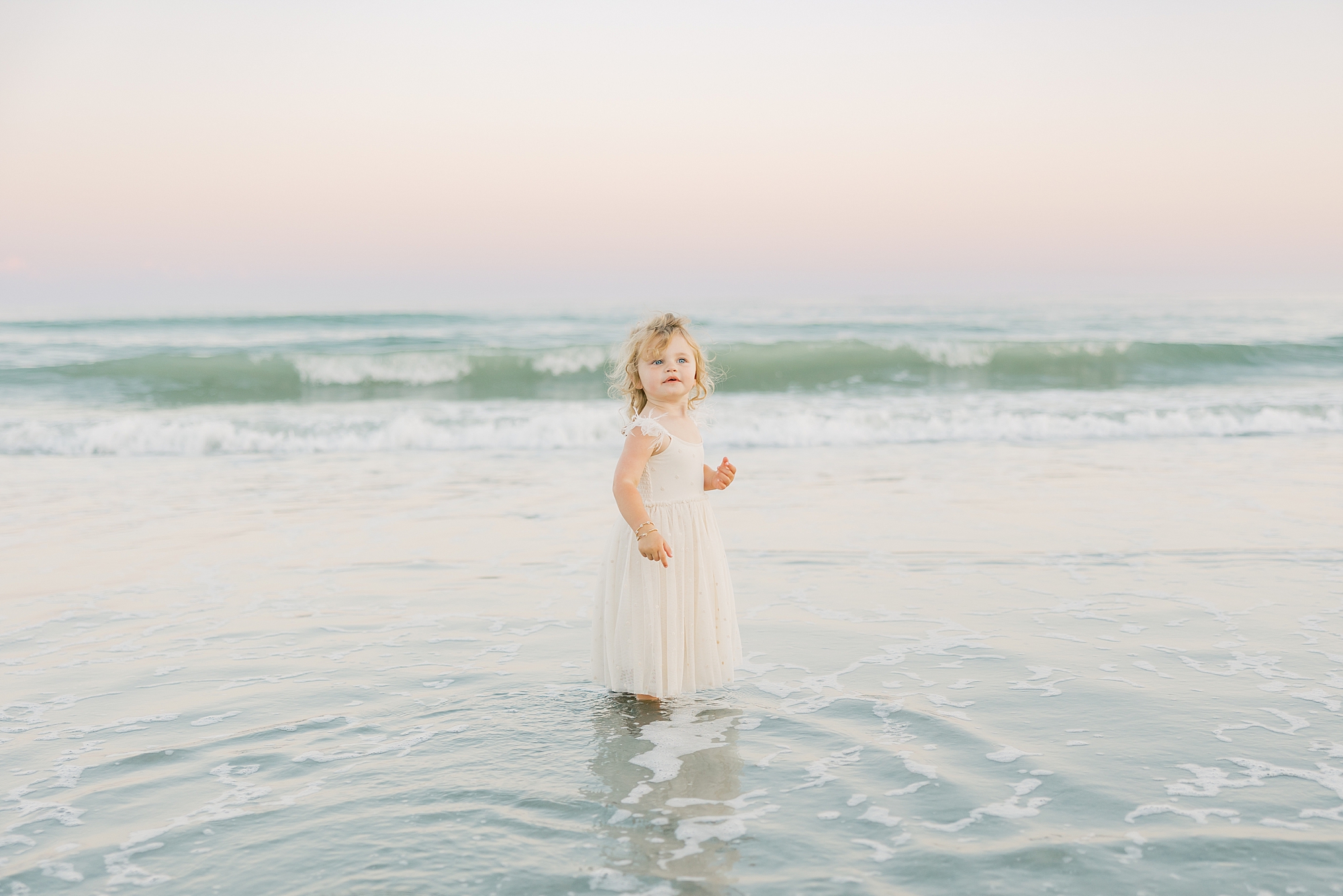 toddler turns to look standing in shallow water during Charleston beach family photos