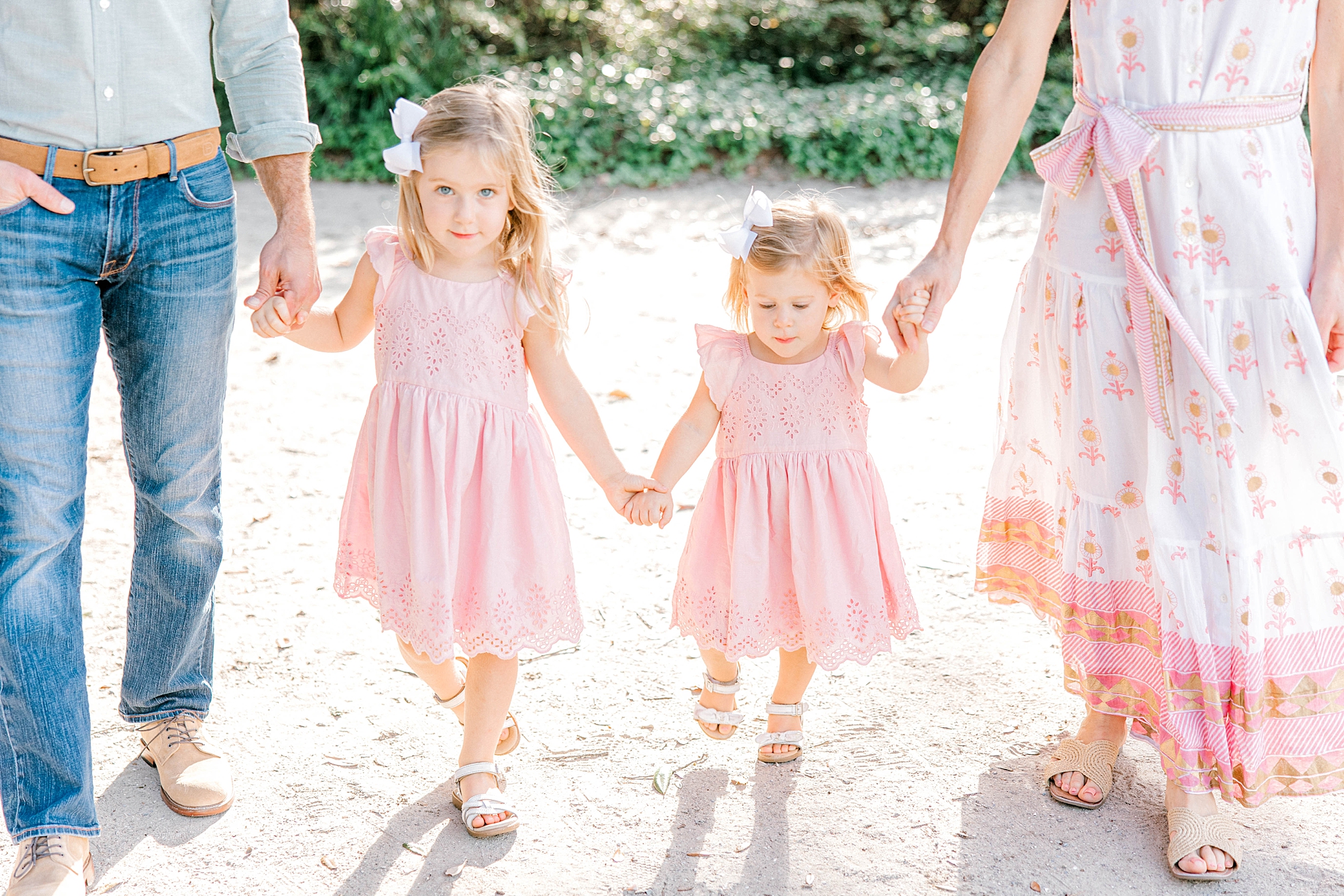sisters in pink dresses hold hands walking with parents 