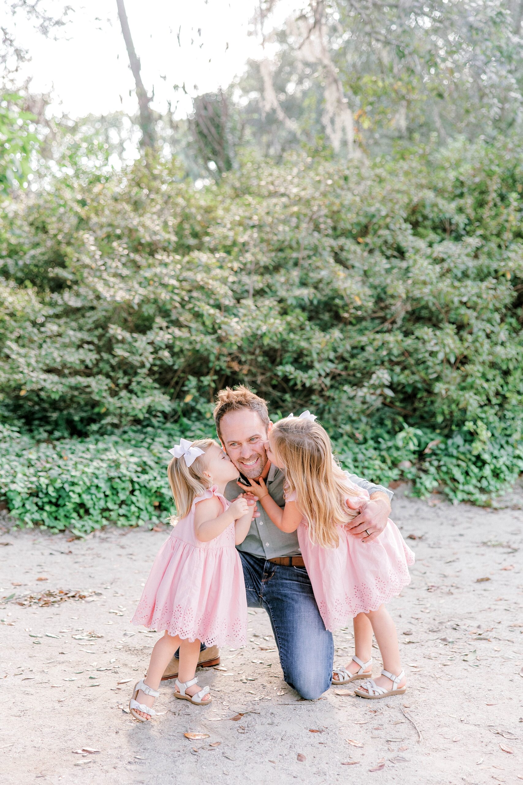 girls in pink dresses kiss dad's cheeks