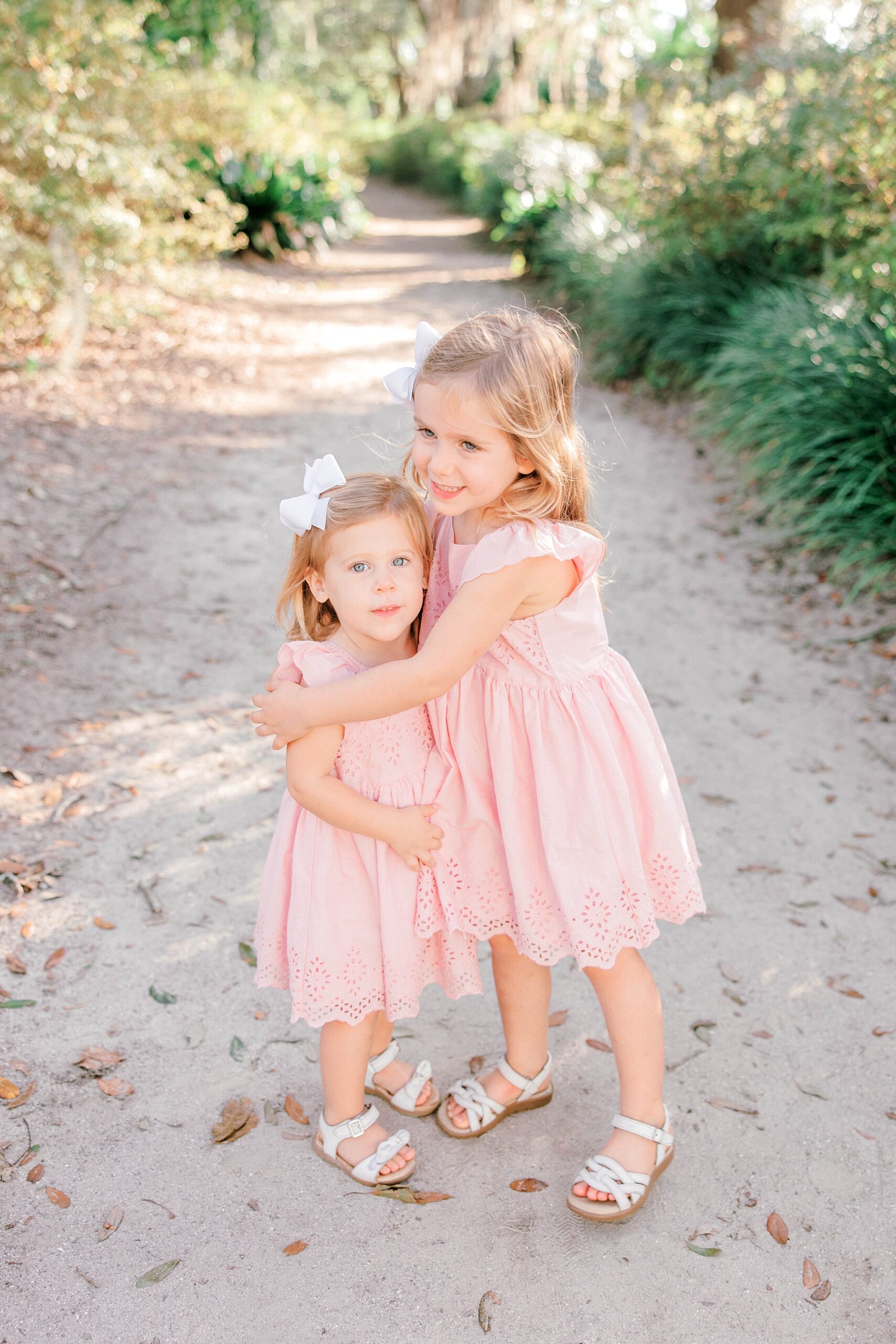 sisters in pink dresses hug on path during Hampton Park family portraits