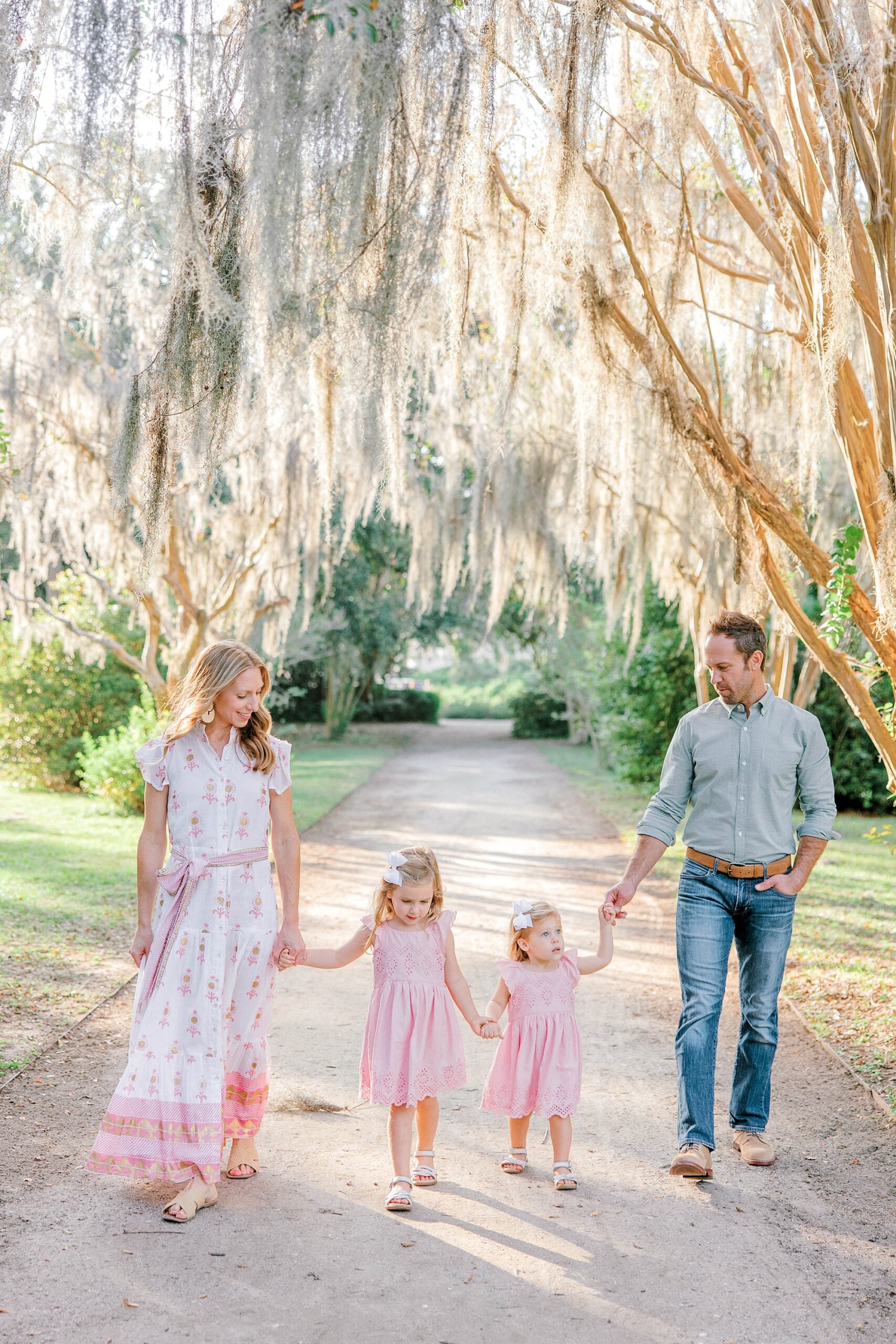 family of four holds hands walking under Spanish moss during Hampton Park family portraits