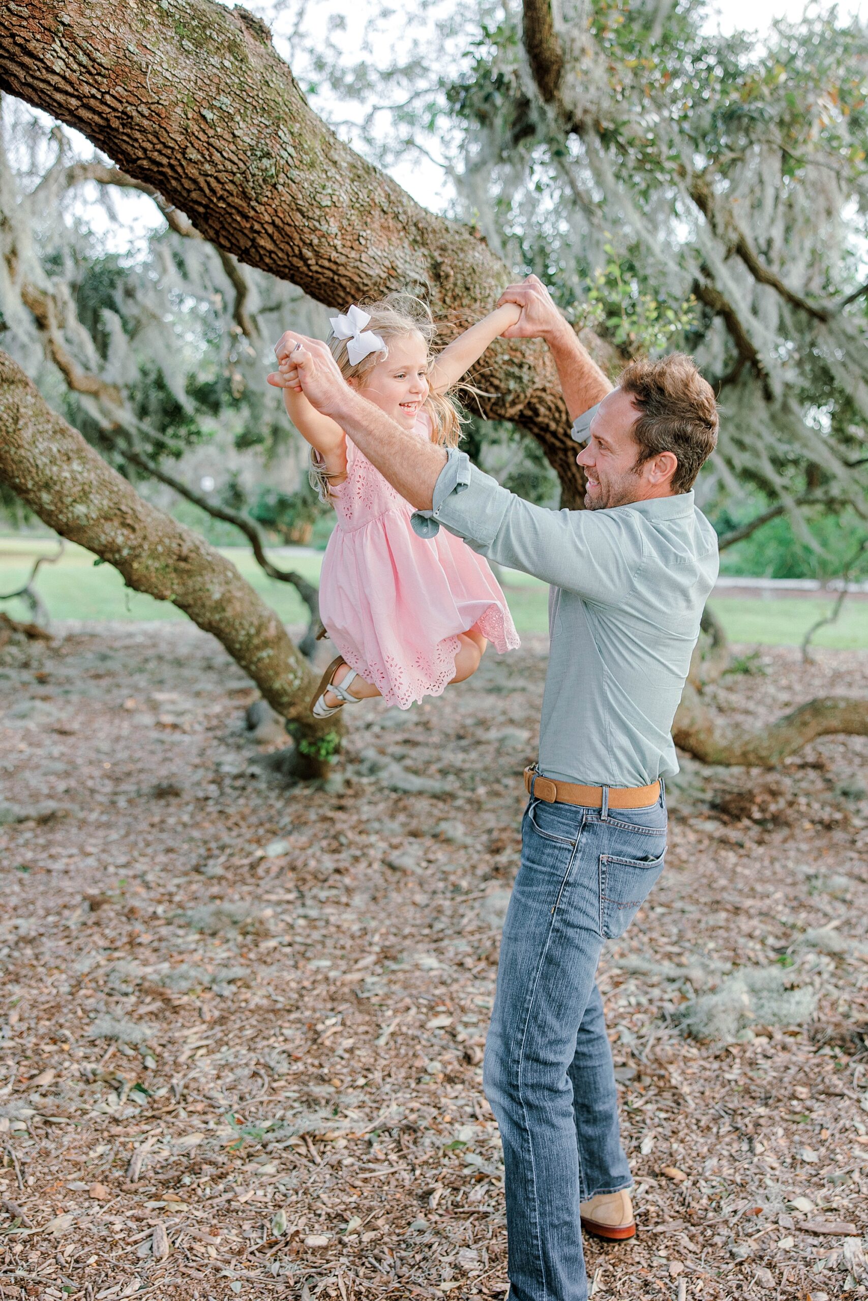 dad swings daughter around by tree during Hampton Park family portraits