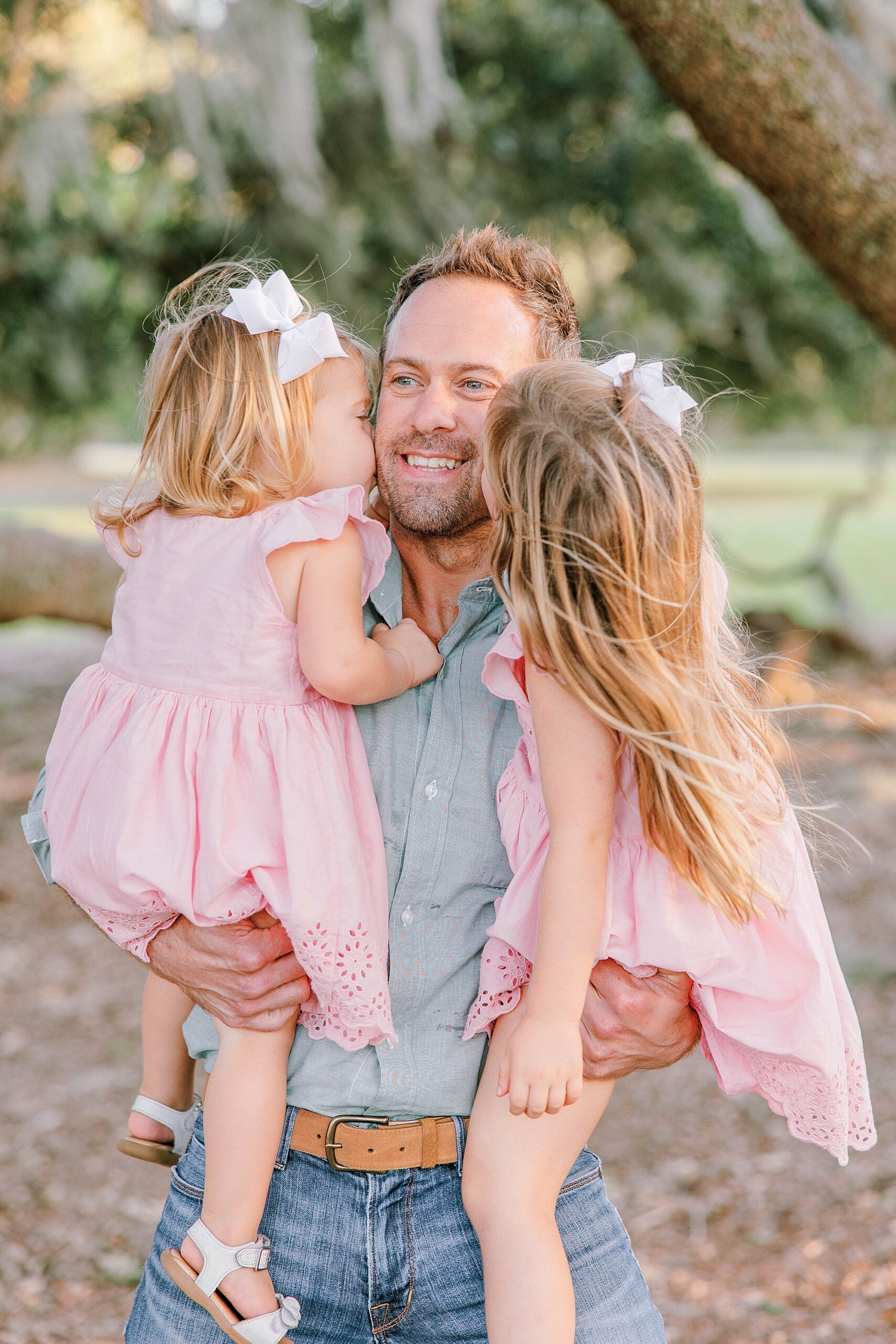 two daughters in pink dresses hug dad kissing his cheek during Hampton Park family portraits