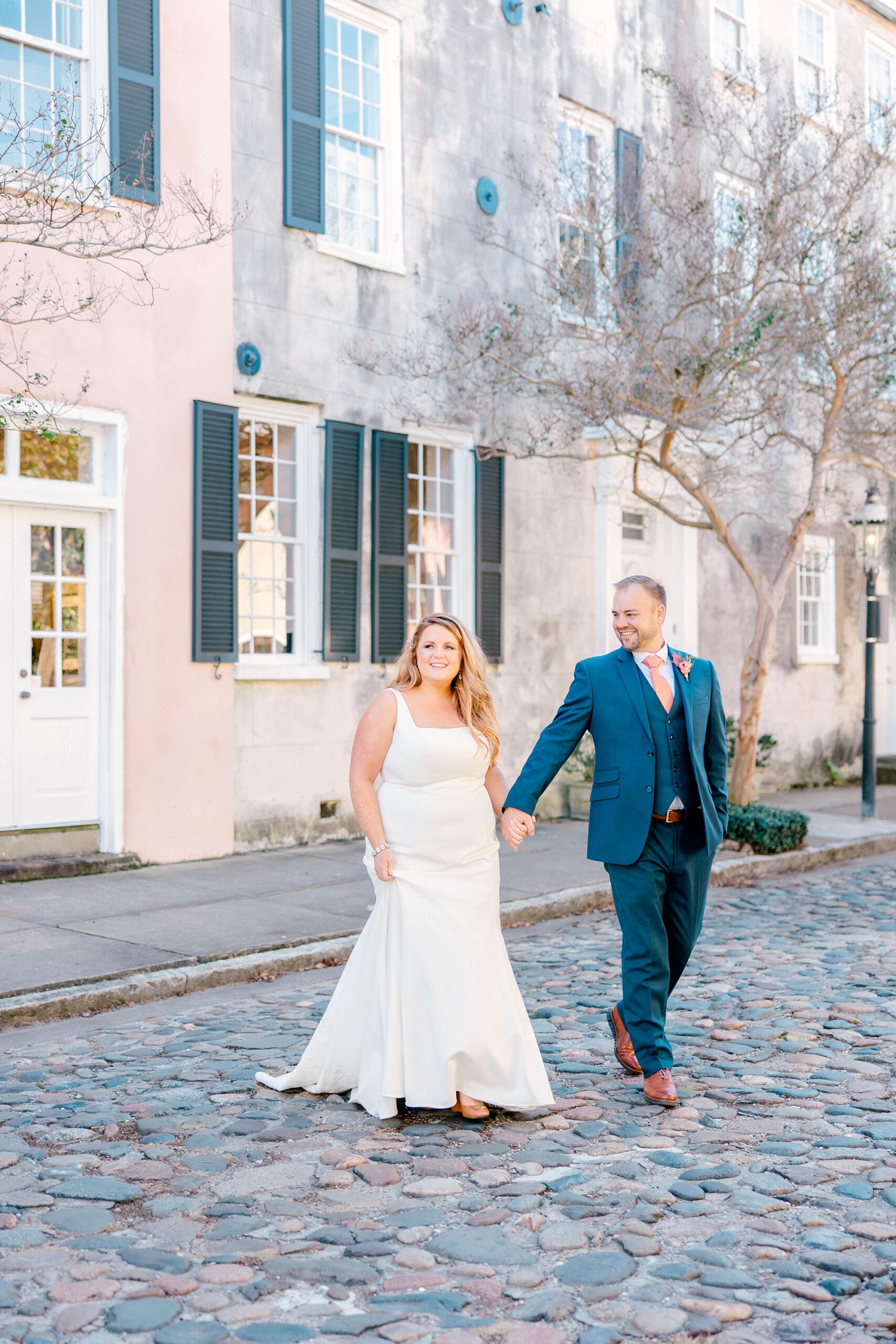 bride and groom hold hands walking across cobblestone street in Charleston SC
