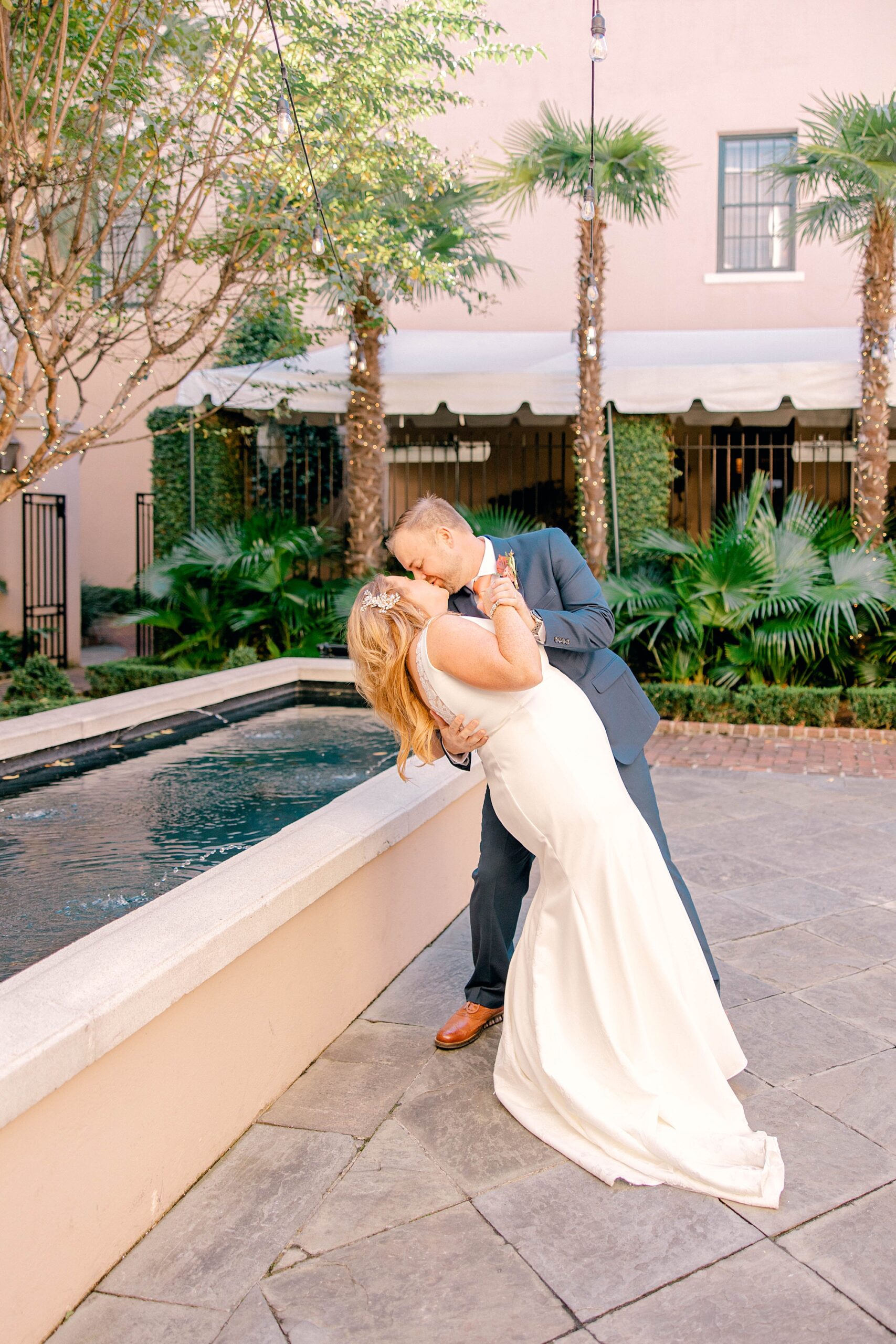 groom in navy suit dips bride kissing in her in courtyard at Planter's Inn