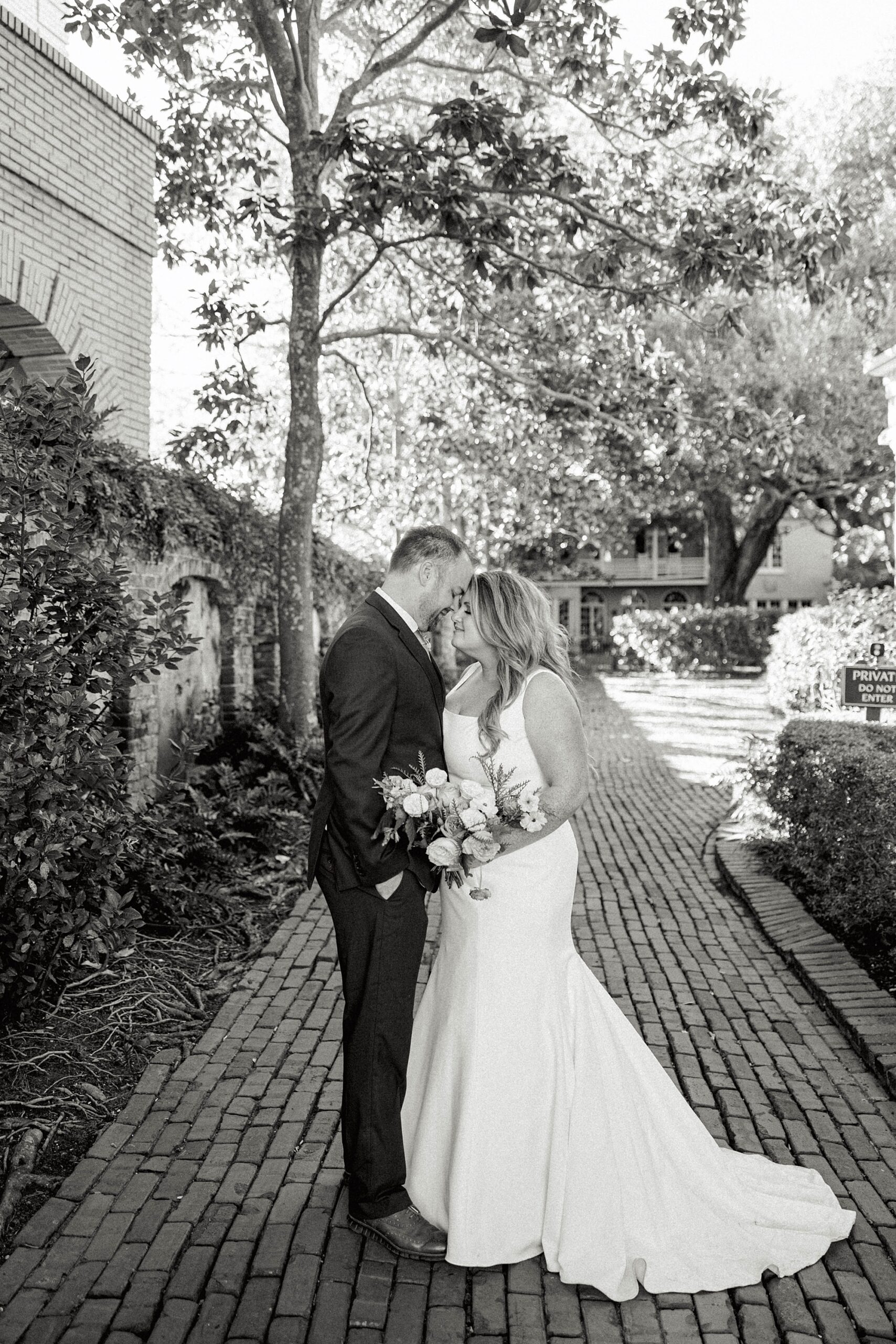black and white portrait of bride and groom leaning for a kiss on cobblestone street