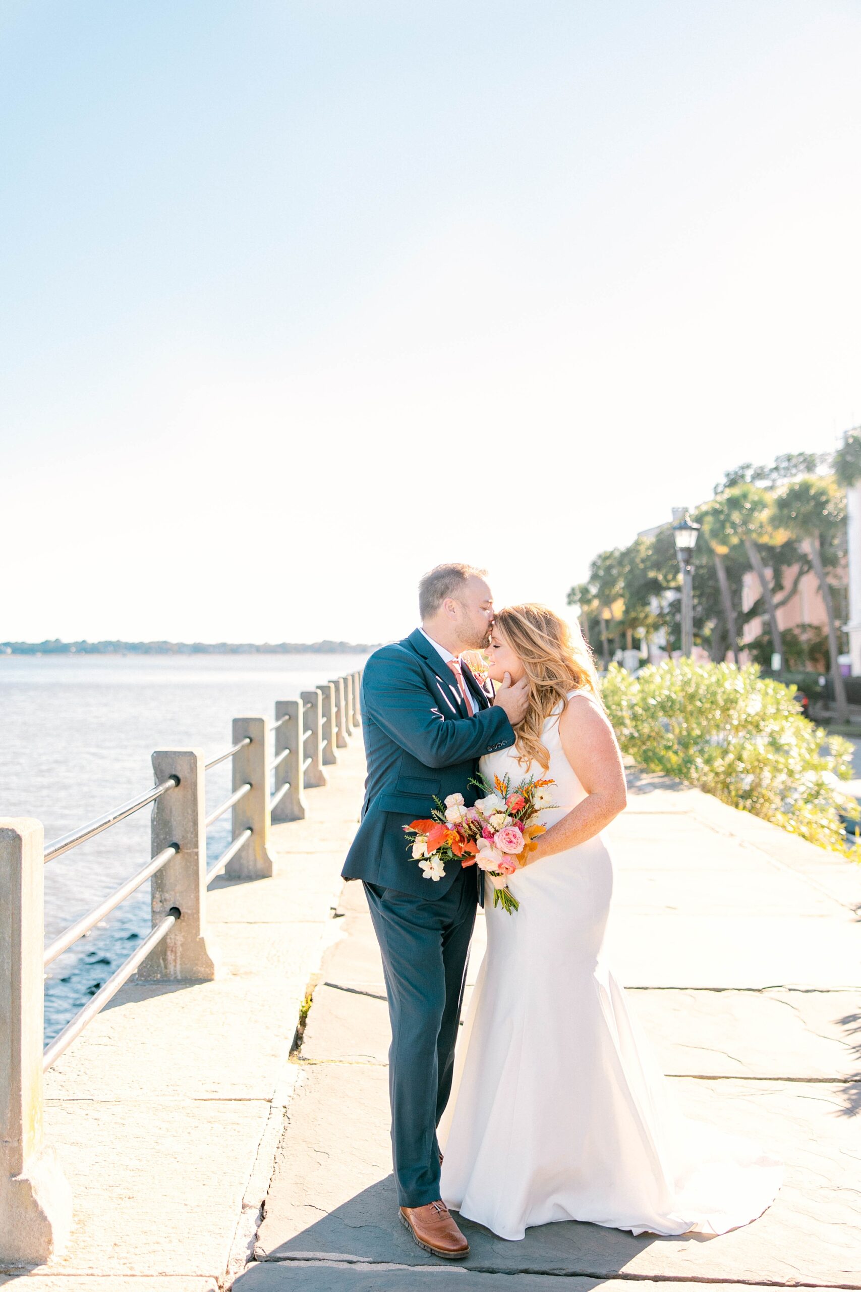 groom kisses bride's forehead along waterfront in Charleston SC