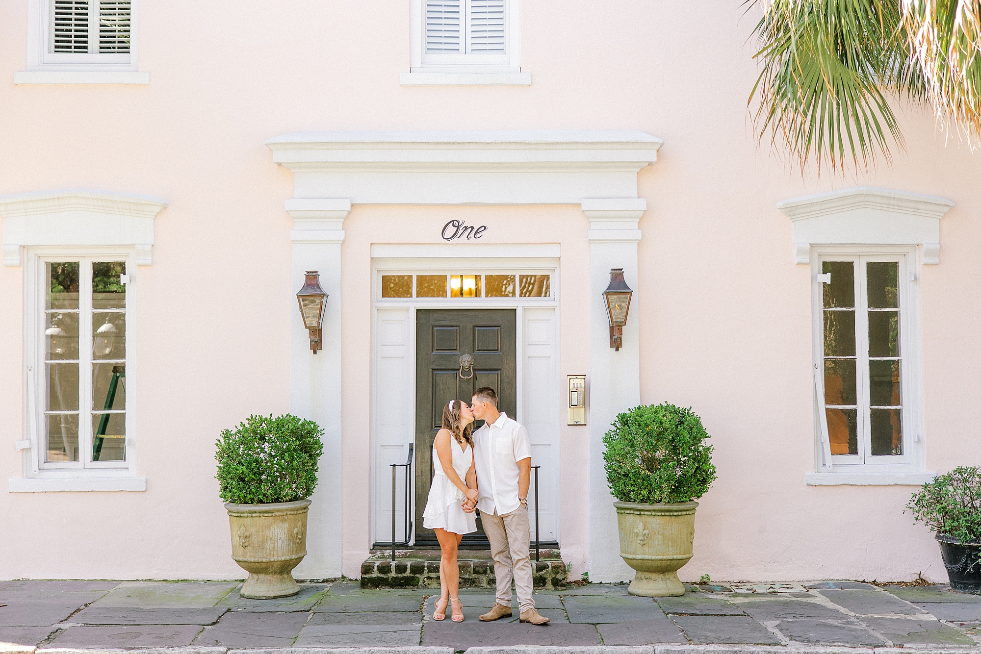 couple kisses in front of home with peach walls in Charleston SC