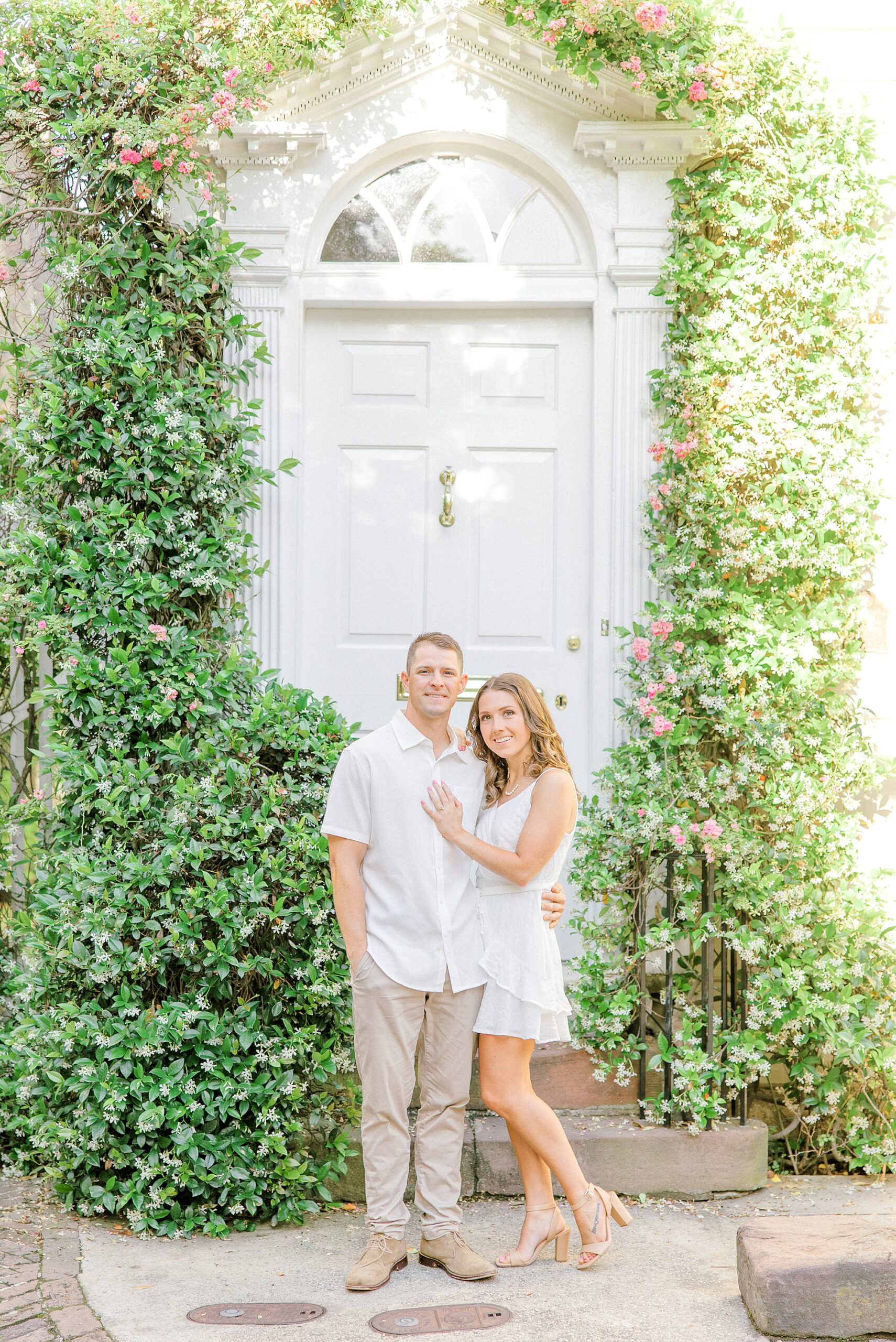 couple hugs in front of white door with ivory growing on the sides in Historic Downtown Charleston