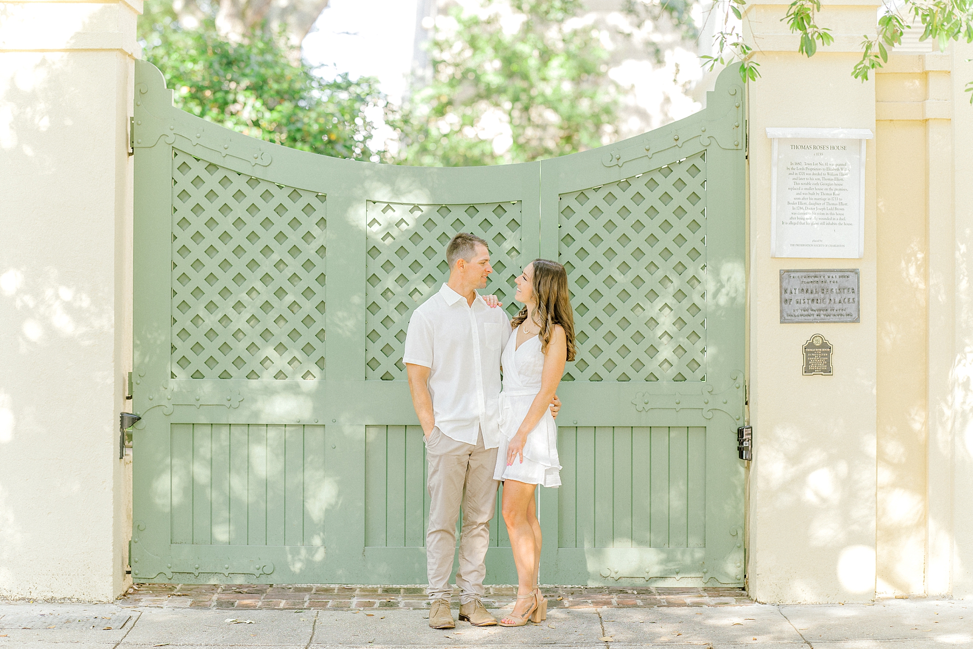 engaged couple holds hands by green gate in Historic Downtown Charleston