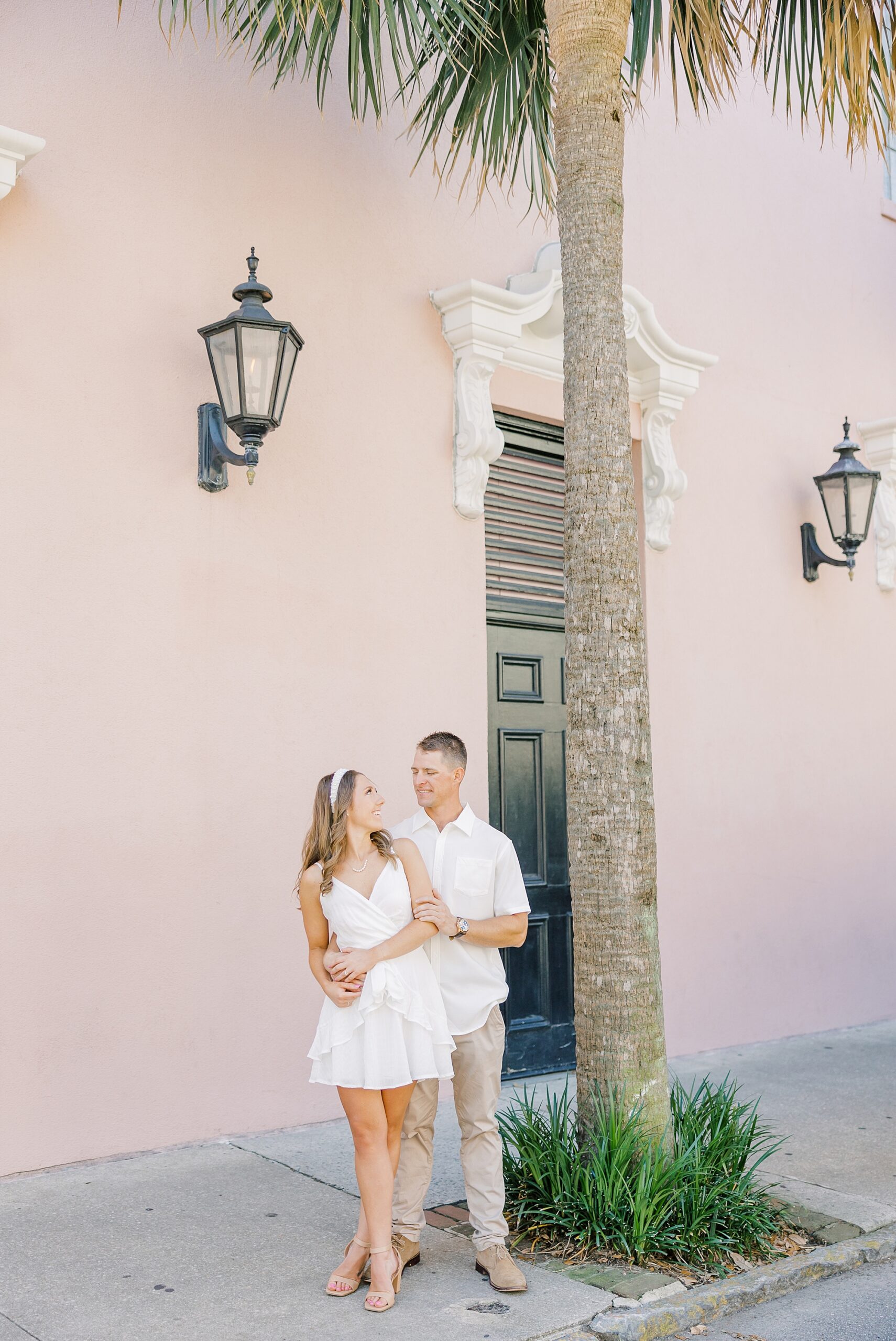 couple hugs by pink wall in Charleston SC with palm tree nearby