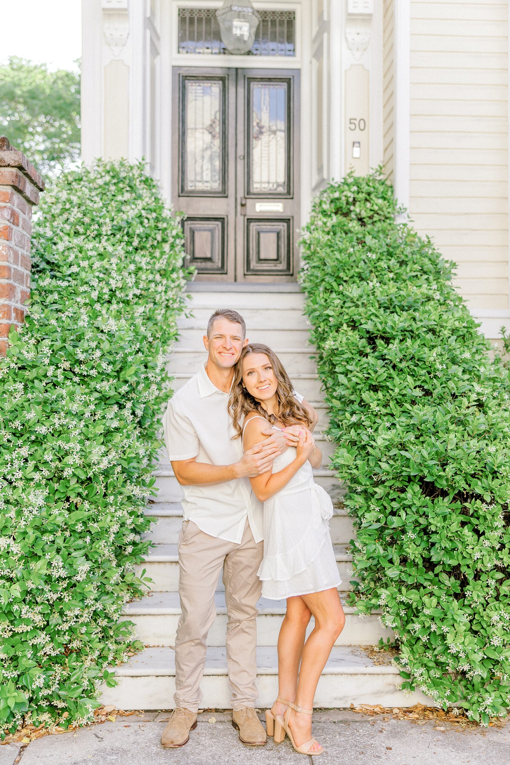 woman in white dress leans against man's chest in front of ivy covered walls