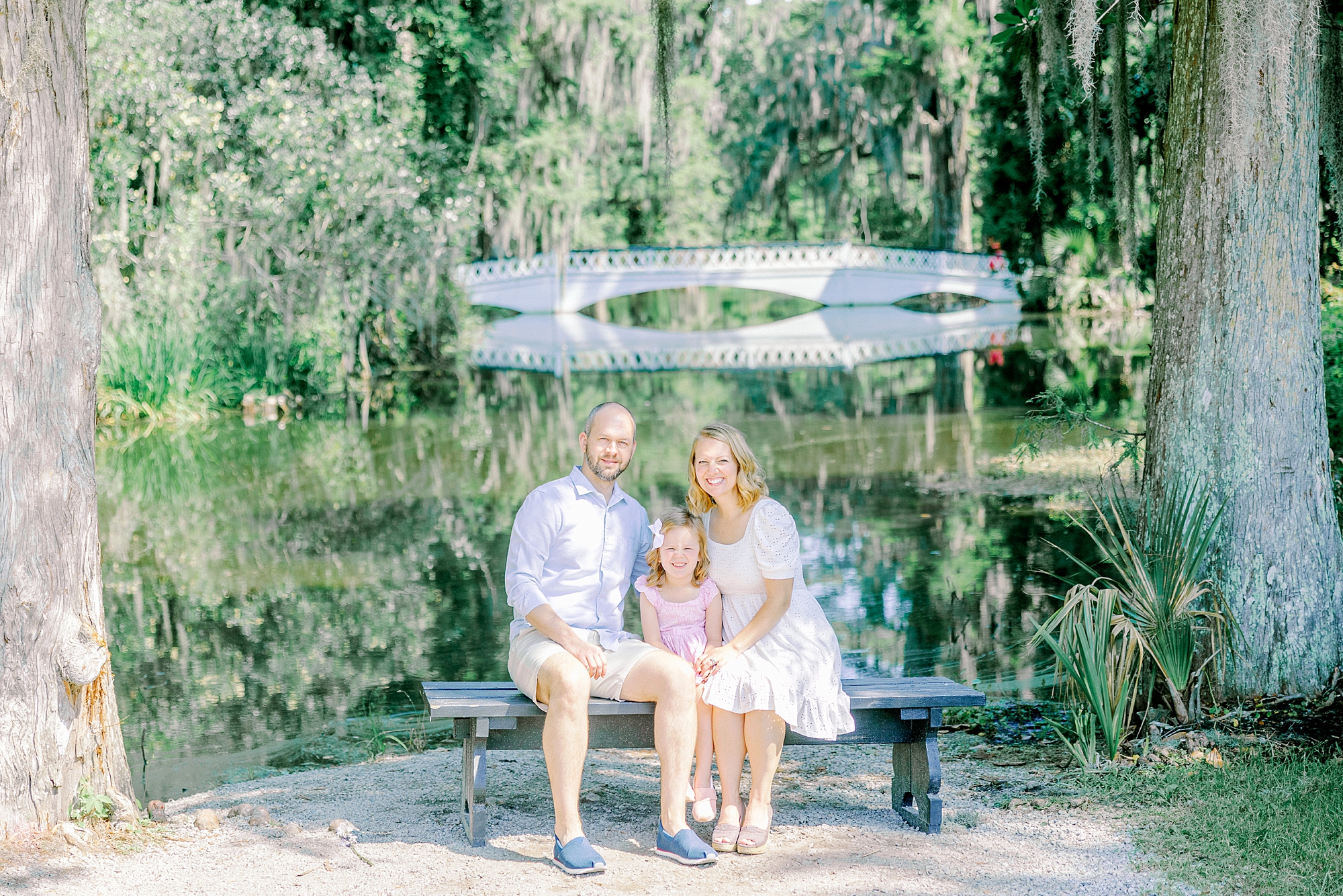 family sits on bench in front of bridge during Magnolia Gardens family portraits
