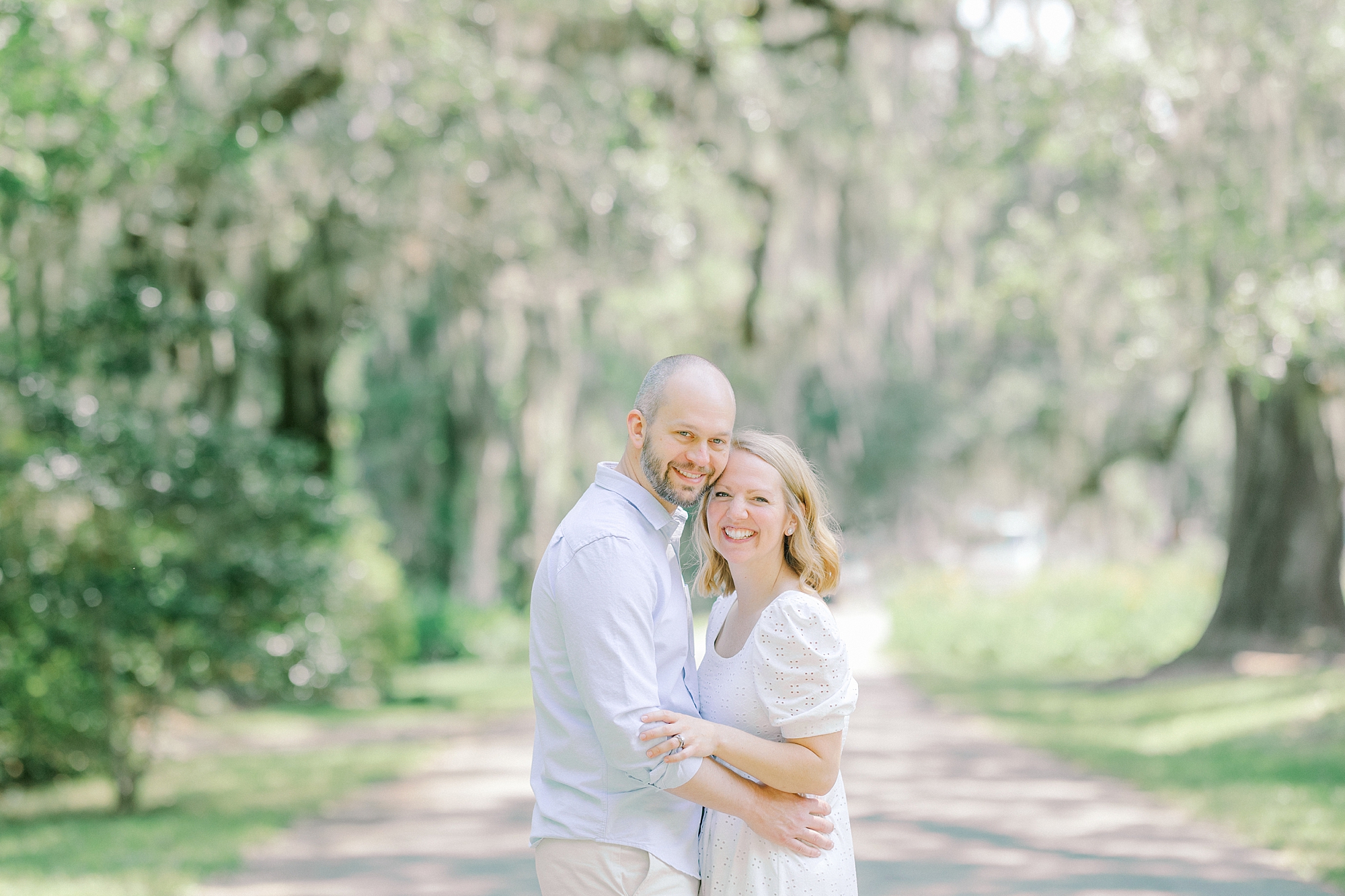 man hugs wife in front of weeping willow and Spanish moss
