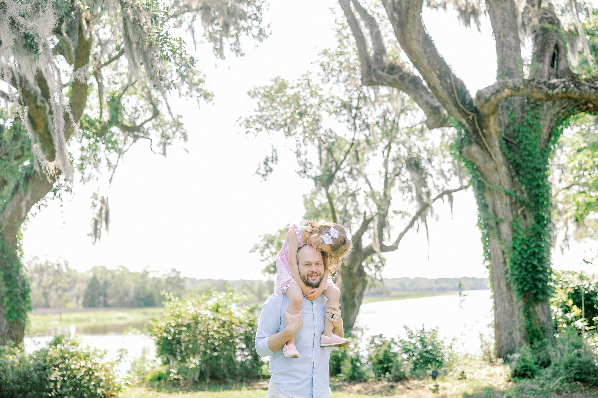 dad walks with daughter on shoulders during Magnolia Gardens family portraits