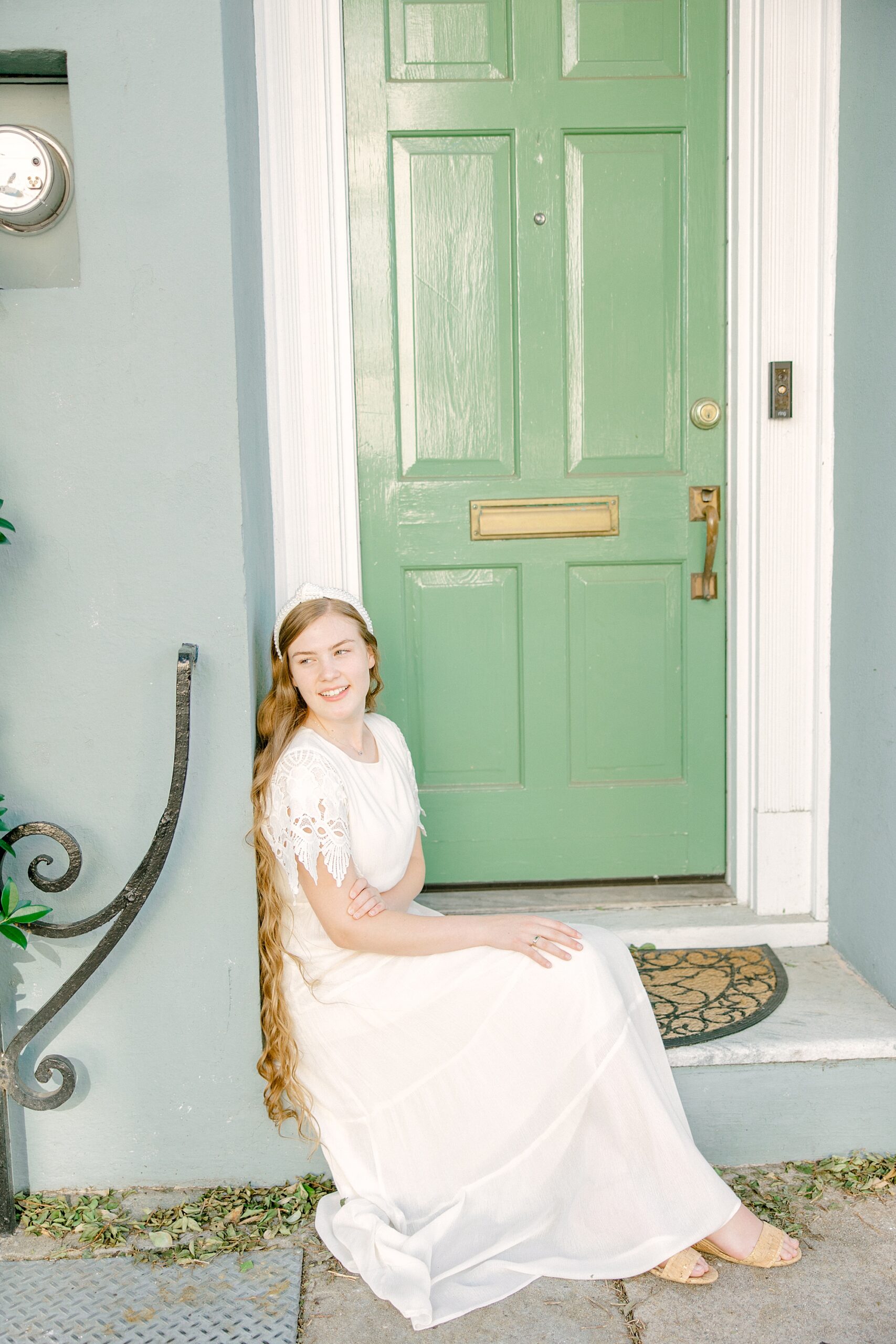 girl sits in front of green doors on Rainbow Row in Charleston SC