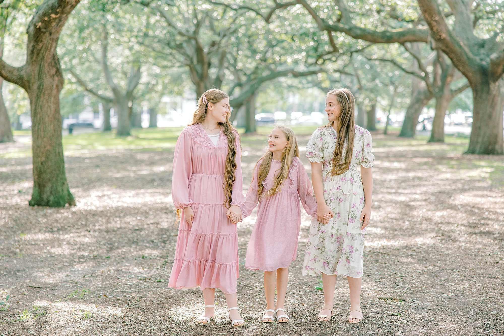 three sisters hold hands under oak trees in White Point Garden