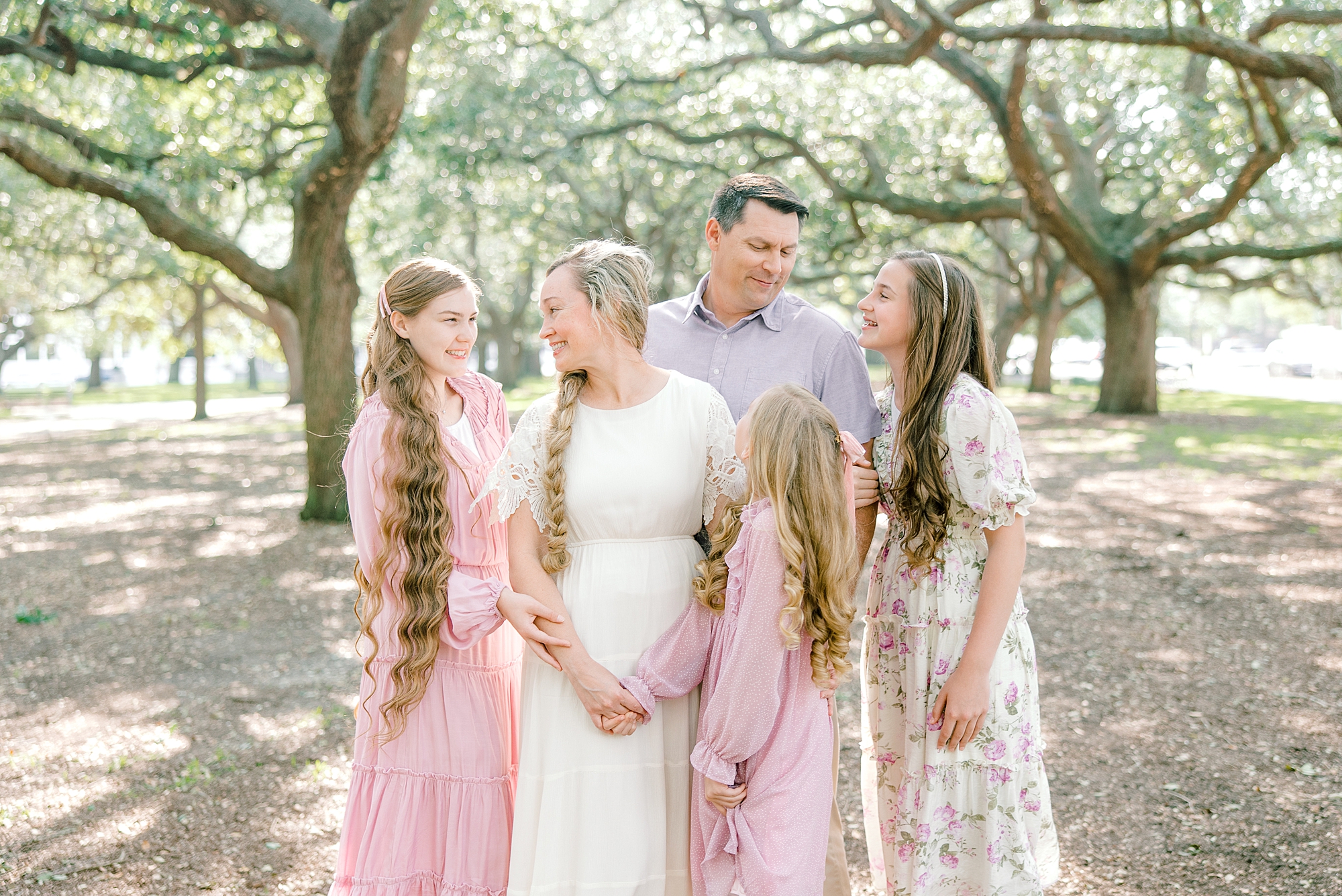 parents smile with three daughters in pink gowns in Whitepoint Garden in Charleston