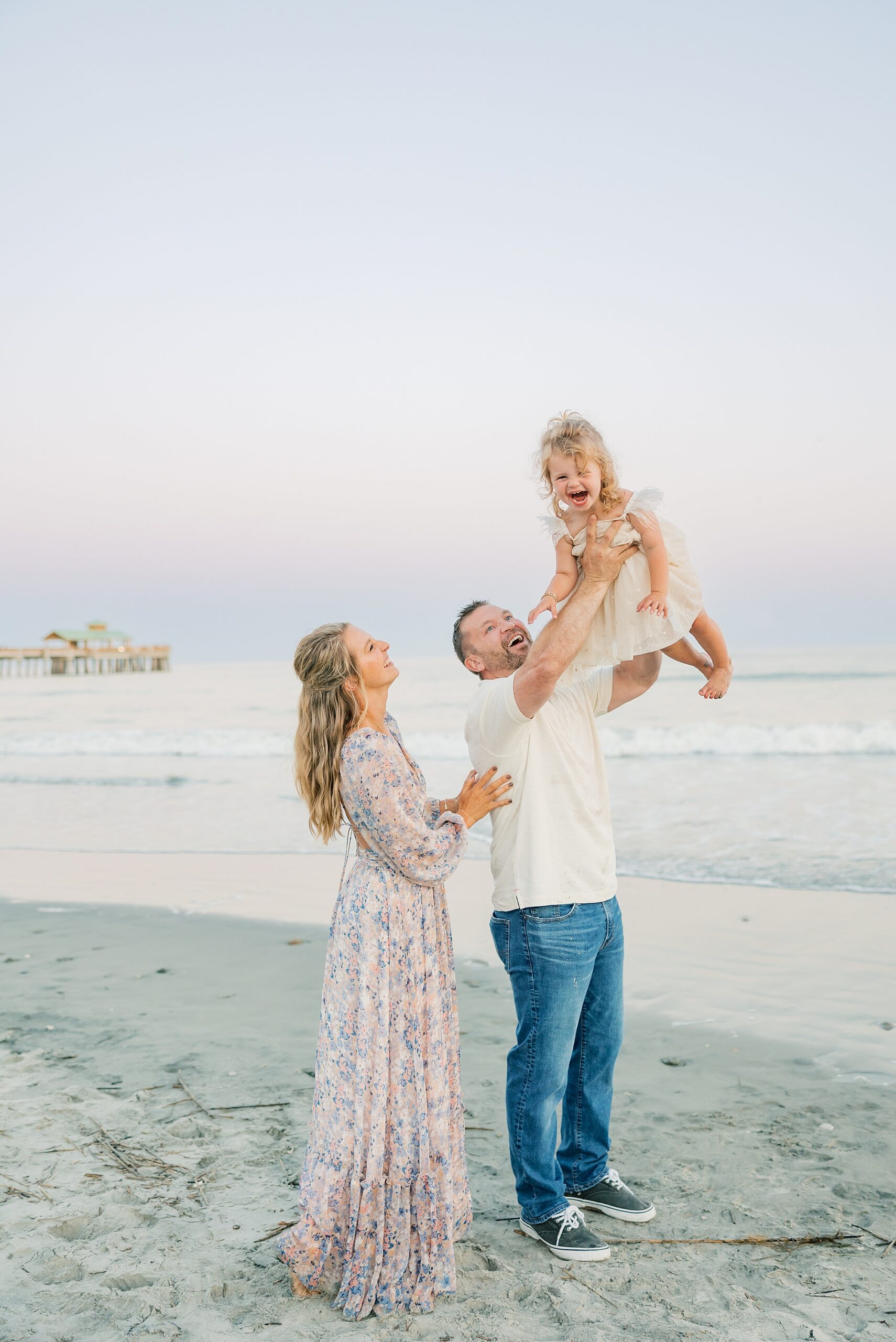 girl laughs with dad holding her in the air during Folly Beach family portraits