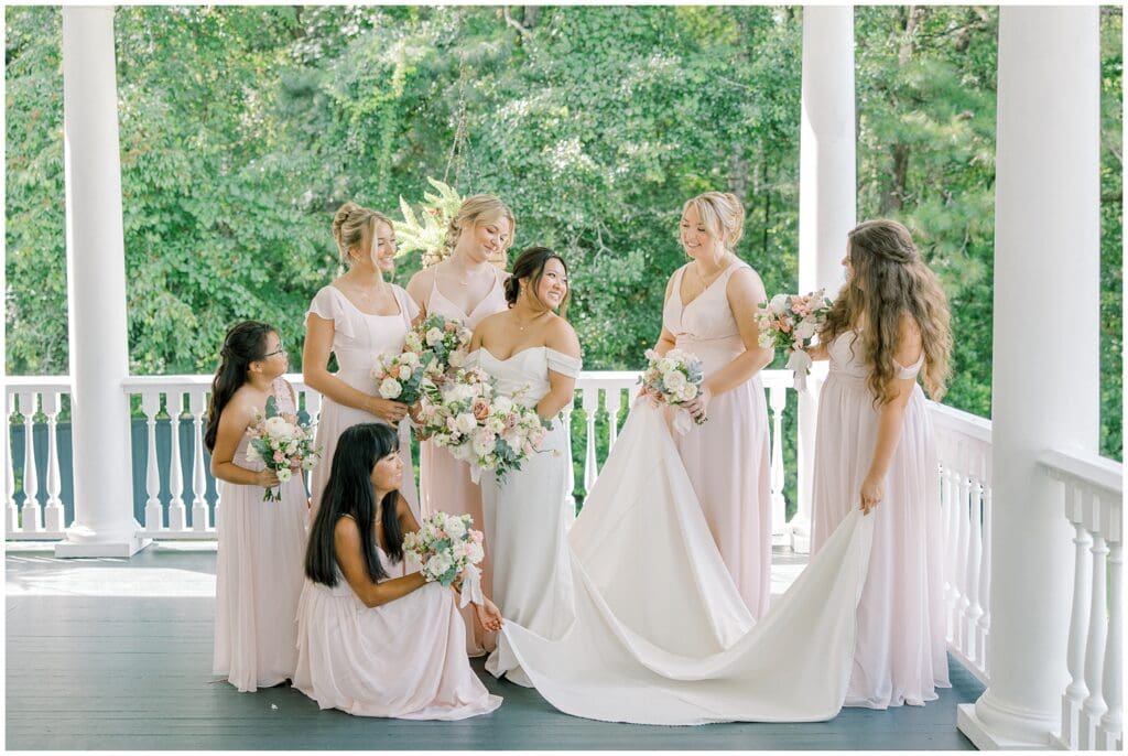 Bride in chic off-the-shoulder gown smiling with bridesmaids in blush dresses on the porch of Old Wide Awake Plantation in Charleston.